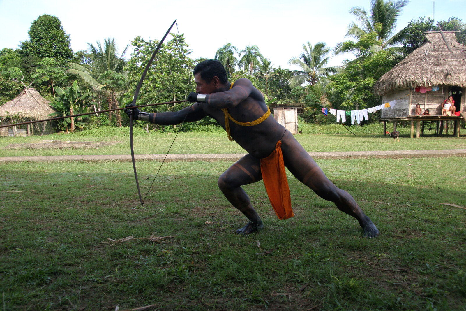Emberá man with traditional jagua body paint demonstrating archery