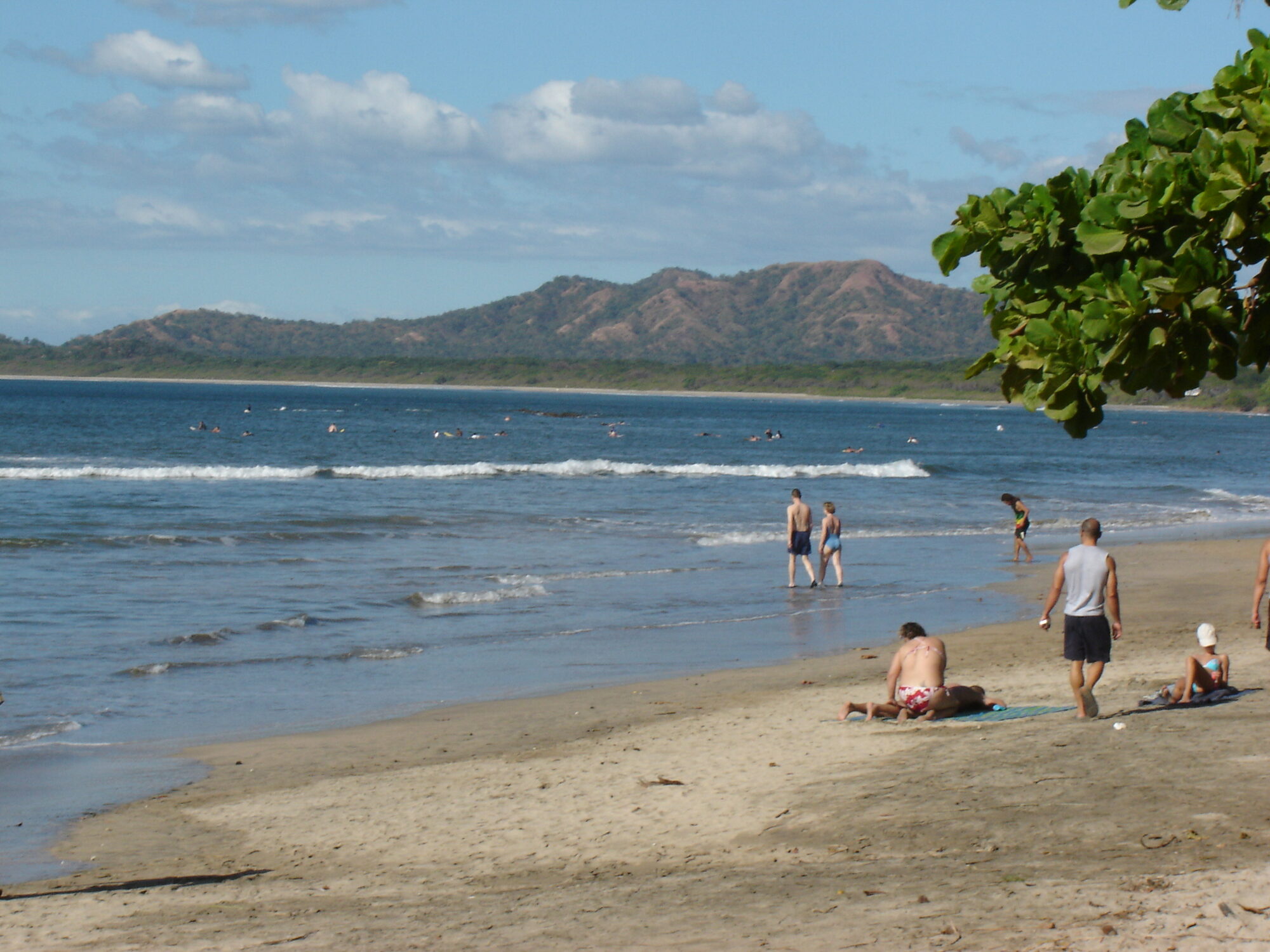 Beach scene at Tamarindo, Costa Rica showing tourists on the sand with characteristic dry forest hills of Guanacaste in the background